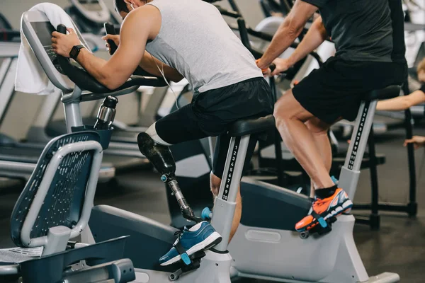 Спортсмен с искусственной ногой тренируется на стационарном велосипеде в тренажерном зале — стоковое фото