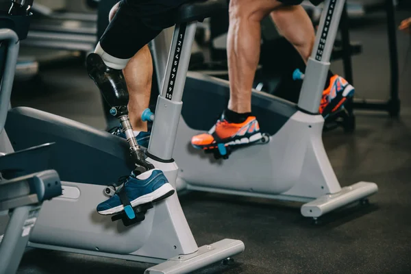 Schnappschuss von Sportler mit Beinprothese beim Training auf stationärem Fahrrad im Fitnessstudio — Stockfoto