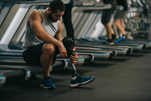 Schöner junger Sportler mit künstlichem Bein sitzt im Fitnessstudio auf dem Laufband — Stockfoto