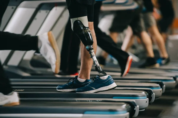 Cropped shot of sportsman with artificial leg running on treadmill at gym with other people — Stock Photo