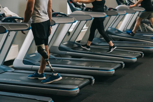 Erschossener Mann mit künstlichem Bein läuft mit anderen Menschen auf Laufbändern in Fitnessstudio — Stockfoto
