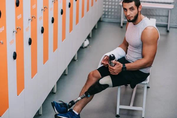 Schöner junger Sportler mit künstlichem Bein sitzt auf Bank in der Umkleidekabine des Fitnessstudios und schaut in die Kamera — Stockfoto