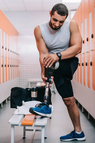 Atlético joven deportista poner en pierna artificial en vestuario gimnasio - foto de stock