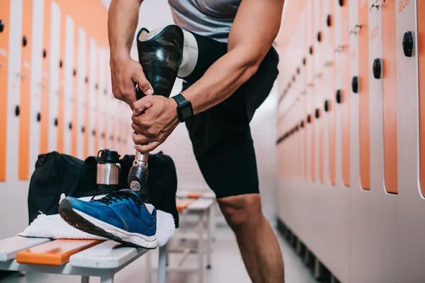 Cropped shot of sportsman putting on artificial leg at gym changing room — Stock Photo