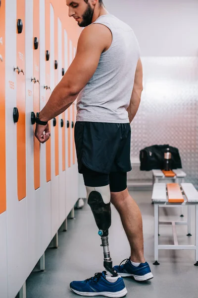 Jovem desportista bonito com armário de abertura de perna artificial com chave elétrica em seu pulso no vestiário ginásio — Fotografia de Stock