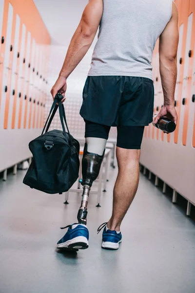 Plan recadré de sportif avec jambe artificielle debout à la salle de gym vestiaire avec bouteille et sac — Photo de stock