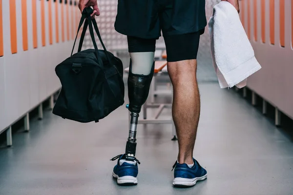 Cropped shot of sportsman with artificial leg standing at gym changing room with towel and bag — Stock Photo