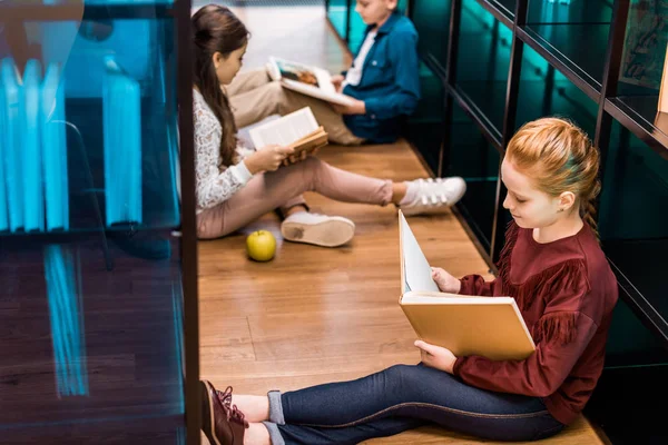 Високий кут зору чарівних школярів, які сидять на підлозі і читають книги в бібліотеці — стокове фото