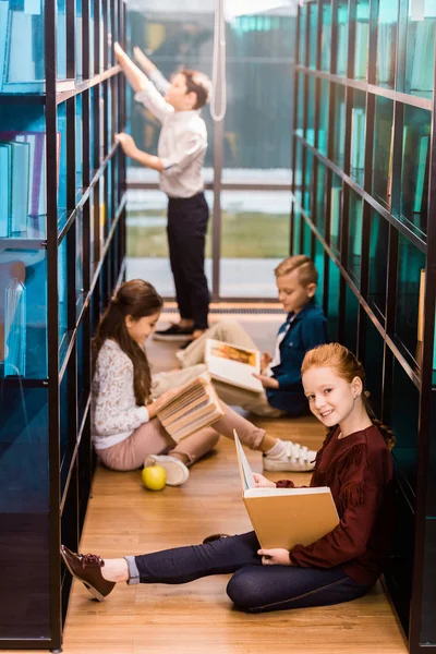 Visão de alto ângulo de adoráveis escolares lendo livros no chão na biblioteca — Fotografia de Stock