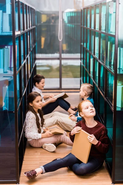 Blick von oben auf entzückende Schulkinder, die Bücher auf dem Fußboden in der Bibliothek lesen — Stockfoto