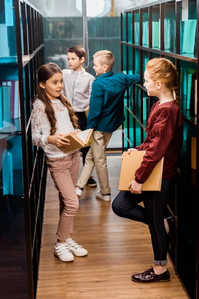 Escolares sosteniendo libros y hablando en la biblioteca - foto de stock