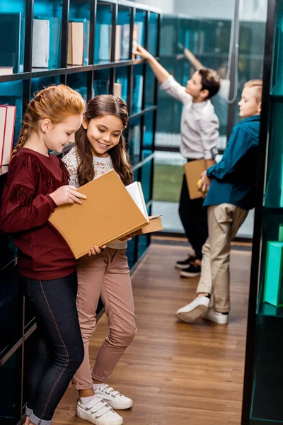 Adorável sorrindo escolares ler livro na biblioteca — Fotografia de Stock