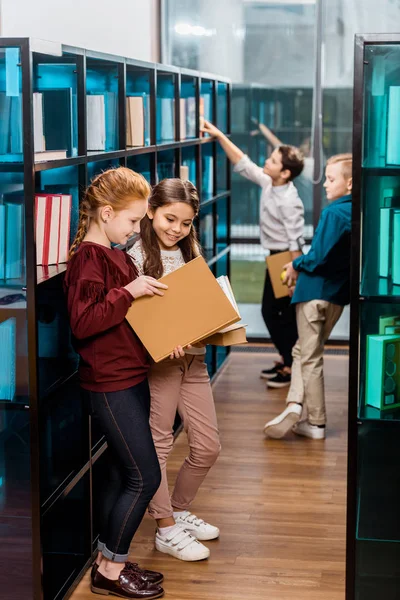Bellissimi scolari sorridenti che leggono libri in biblioteca — Foto stock