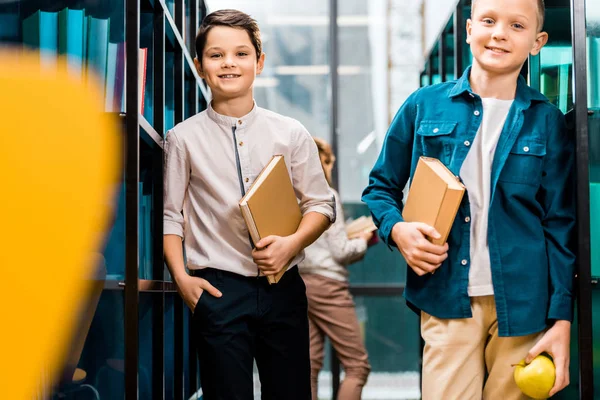 Adorable schoolboys holding books and smiling at camera in library — Stock Photo