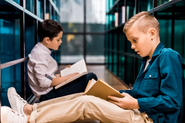 Side view of schoolboys reading books while sitting on floor in library — Stock Photo