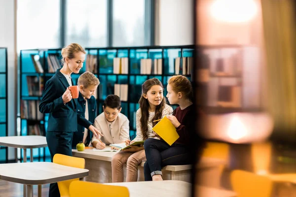 Selective focus of schoolchildren and librarian talking together in library — Stock Photo