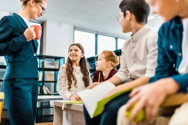 Plan recadré de bibliothécaire souriant parlant avec des écoliers à la bibliothèque — Photo de stock