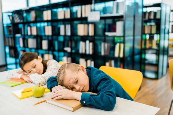 Colegas cansados em óculos dormindo na mesa com livros na biblioteca — Fotografia de Stock