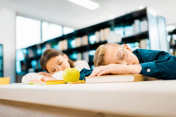 Escolares cansados em óculos dormindo na mesa na biblioteca — Fotografia de Stock