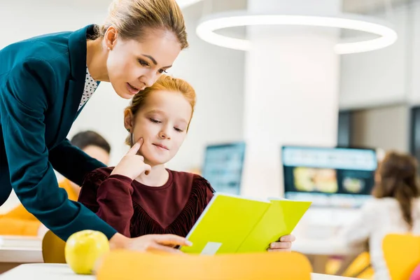 Jovem professora e adorável estudante estudando juntos na biblioteca — Fotografia de Stock