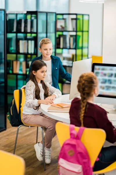 Escolares que usan computadoras de escritorio y estudian juntos en la biblioteca - foto de stock