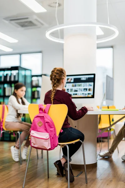 Зосереджені школярки сидять і використовують настільні комп'ютери в бібліотеці — стокове фото