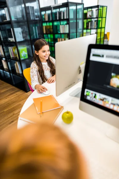 High angle view of adorable smiling schoolchild studying with computer in library — Stock Photo