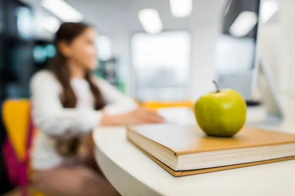 Vue rapprochée de pomme sur livre et écolier assis derrière dans la bibliothèque — Photo de stock