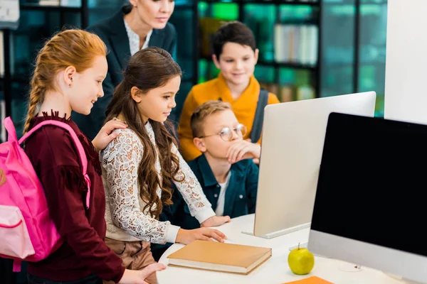 Bonito alunos e bibliotecário usando computador juntos na biblioteca — Fotografia de Stock