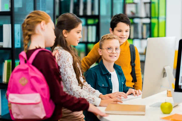 Junge lächelt in die Kamera, während er Computer mit Klassenkameraden in der Bibliothek benutzt — Stockfoto