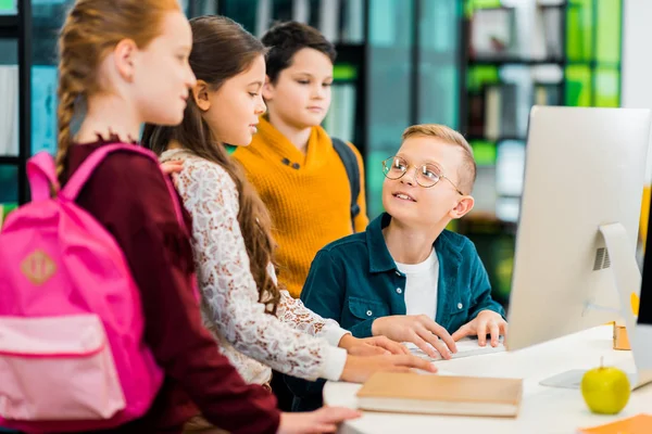 Хлопчик використовує настільний комп'ютер і дивиться на однокласників в бібліотеці — стокове фото