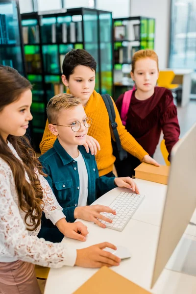 Hochwinkel-Ansicht von entzückend lächelnden Schulkindern mit Desktop-Computer in der Bibliothek — Stockfoto