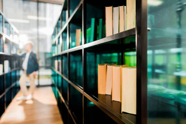 Books on bookshelves and schoolboy standing behind in library — Stock Photo