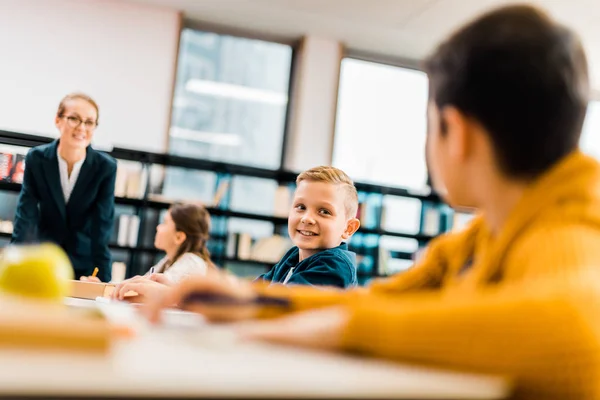 Jovem professor sorridente e alunos estudando juntos na biblioteca — Fotografia de Stock