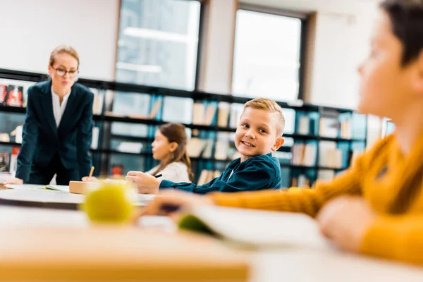 Lehrer schaut auf Schüler, die an Schreibtischen in Bibliothek lernen — Stockfoto