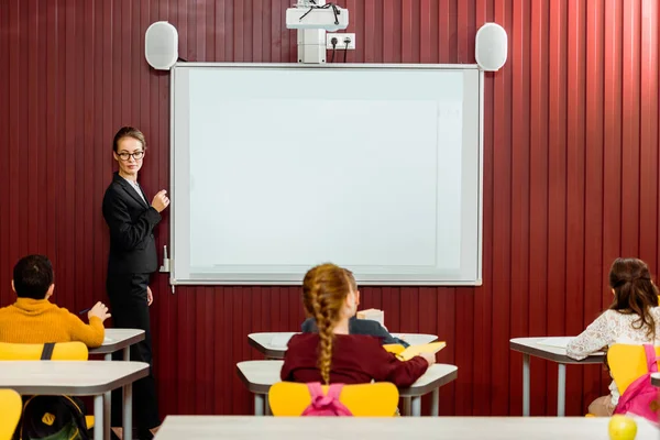 Rückansicht von Schülern, die am Schreibtisch sitzen und Lehrer, die Präsentationen am Whiteboard machen — Stockfoto