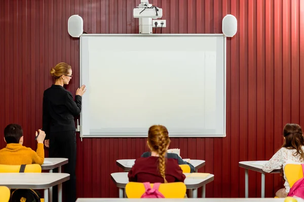 Visão traseira de alunos sentados em mesas e professor fazendo apresentação no quadro branco — Fotografia de Stock