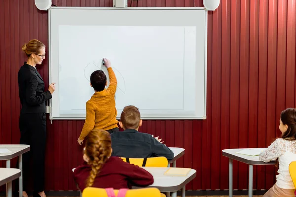 Visão traseira do menino escrevendo no quadro interativo durante a aula — Fotografia de Stock