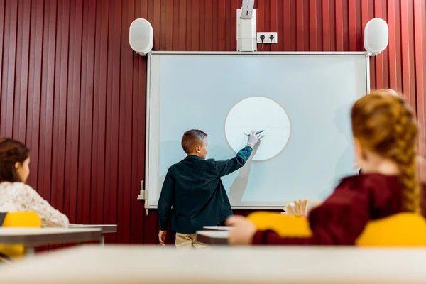 Alunos olhando menino fazendo apresentação no quadro interativo — Fotografia de Stock