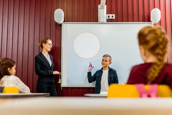 Teacher and schoolchildren looking at boy making presentation at interactive whiteboard — Stock Photo