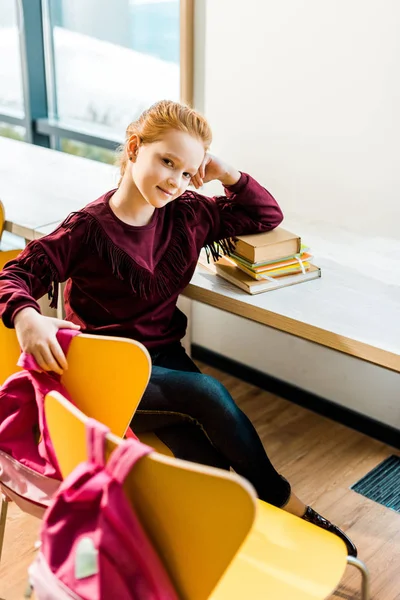 Aus der Vogelperspektive: Schöne Schülerin sitzt mit Büchern am Schreibtisch und lächelt in die Kamera — Stockfoto