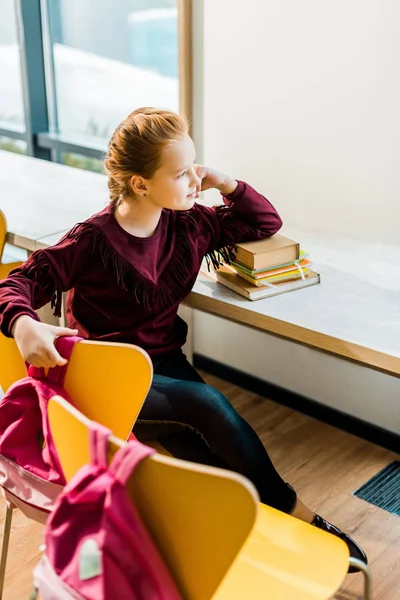 Vista ad alto angolo di bella scolaretta seduta alla scrivania con libri e guardando la finestra — Foto stock