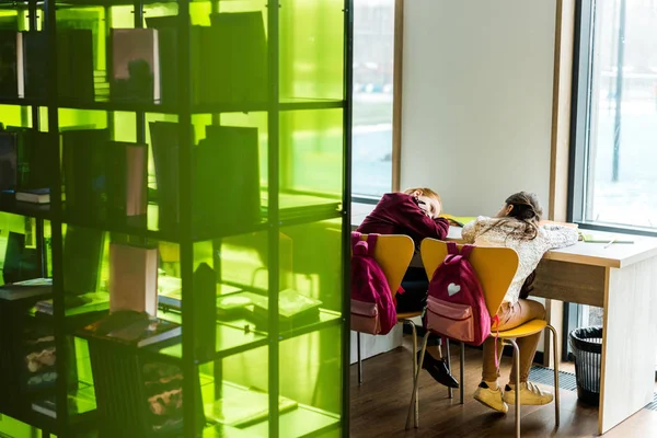 Rückansicht gelangweilter Schülerinnen, die auf dem Tisch in der Bibliothek liegen — Stockfoto