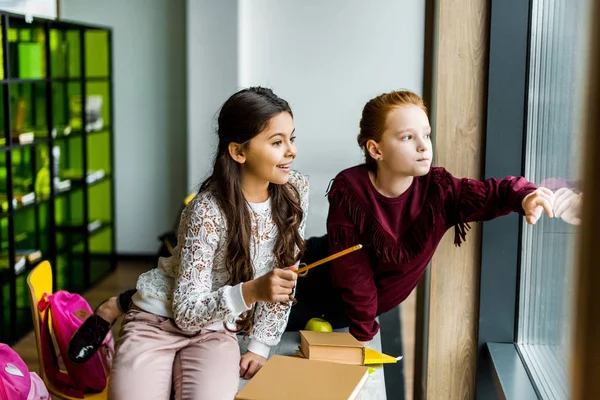 Cute schoolgirls sitting on desk and looking at window — Stock Photo