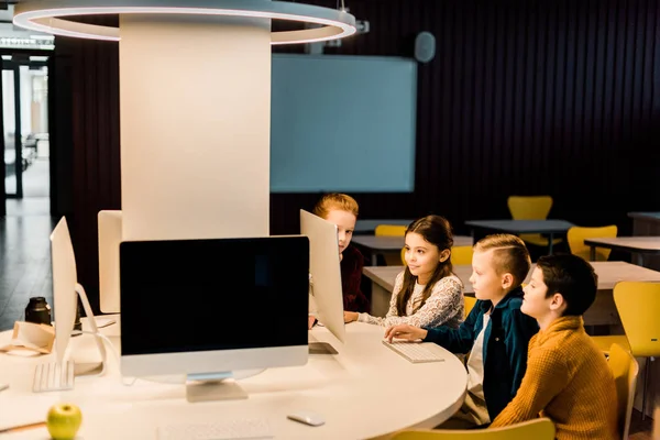 Adorable schoolchildren sitting and using desktop computer together in modern library — Stock Photo