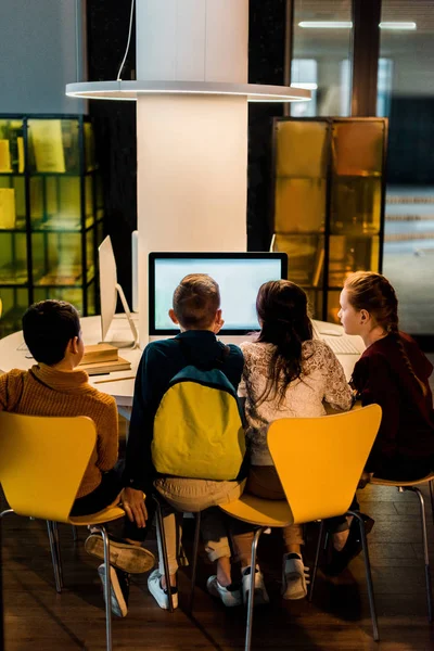 Back view of four schoolchildren using computers in modern library — Stock Photo