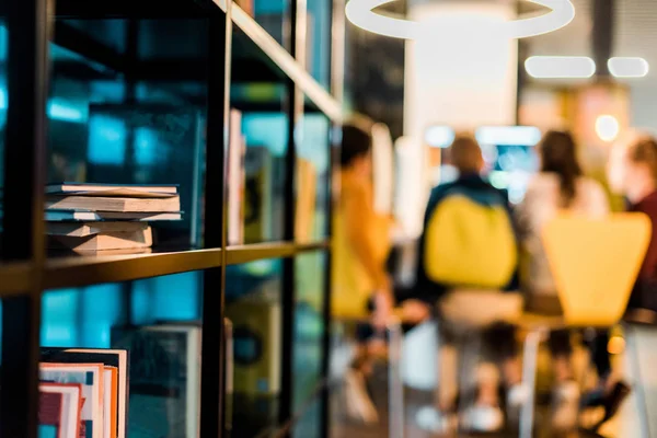 Books on bookshelves and schoolchildren sitting behind in library — Stock Photo