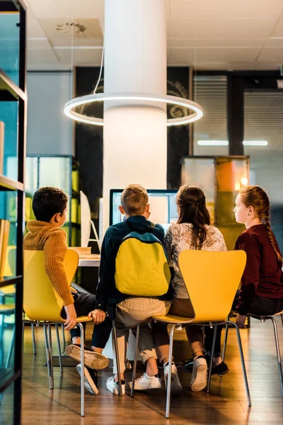 Vista trasera de cuatro escolares que usan computadoras en la biblioteca moderna - foto de stock