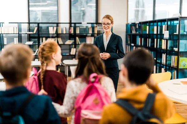 Back view of schoolkids with backpacks looking at female librarian — Stock Photo