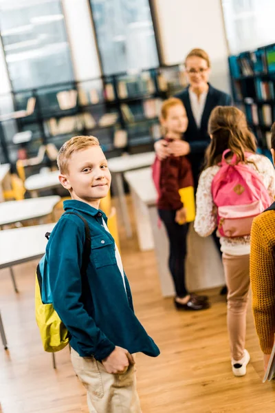 Schüler mit Rucksack schaut in Kamera, während er mit Klassenkameraden die Bibliothek besucht — Stockfoto